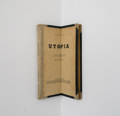 Zdjęcie przedstawia przeciętą wzdłuż na pół i umieszczoną w rogu sali książkę Tomasza Morusa „Utopia”