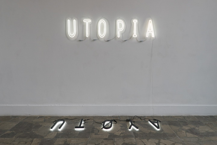 Na ścianie umieszczony jest obiekt artystyczny, świecący na biało neon. Neon składa się z pojedynczych liter, składających się na napis: UTOPIA. Pod spodem na podłodze znajduje się drugi, przypominający lustrzane odbicie neon składający się na napis UTOYA.