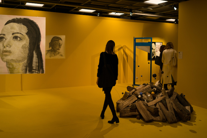 sala pomalowana na żółto, w środku zwiedzająca osoba, po lewej portrety kobiecie, po prawej instalacja z drewna